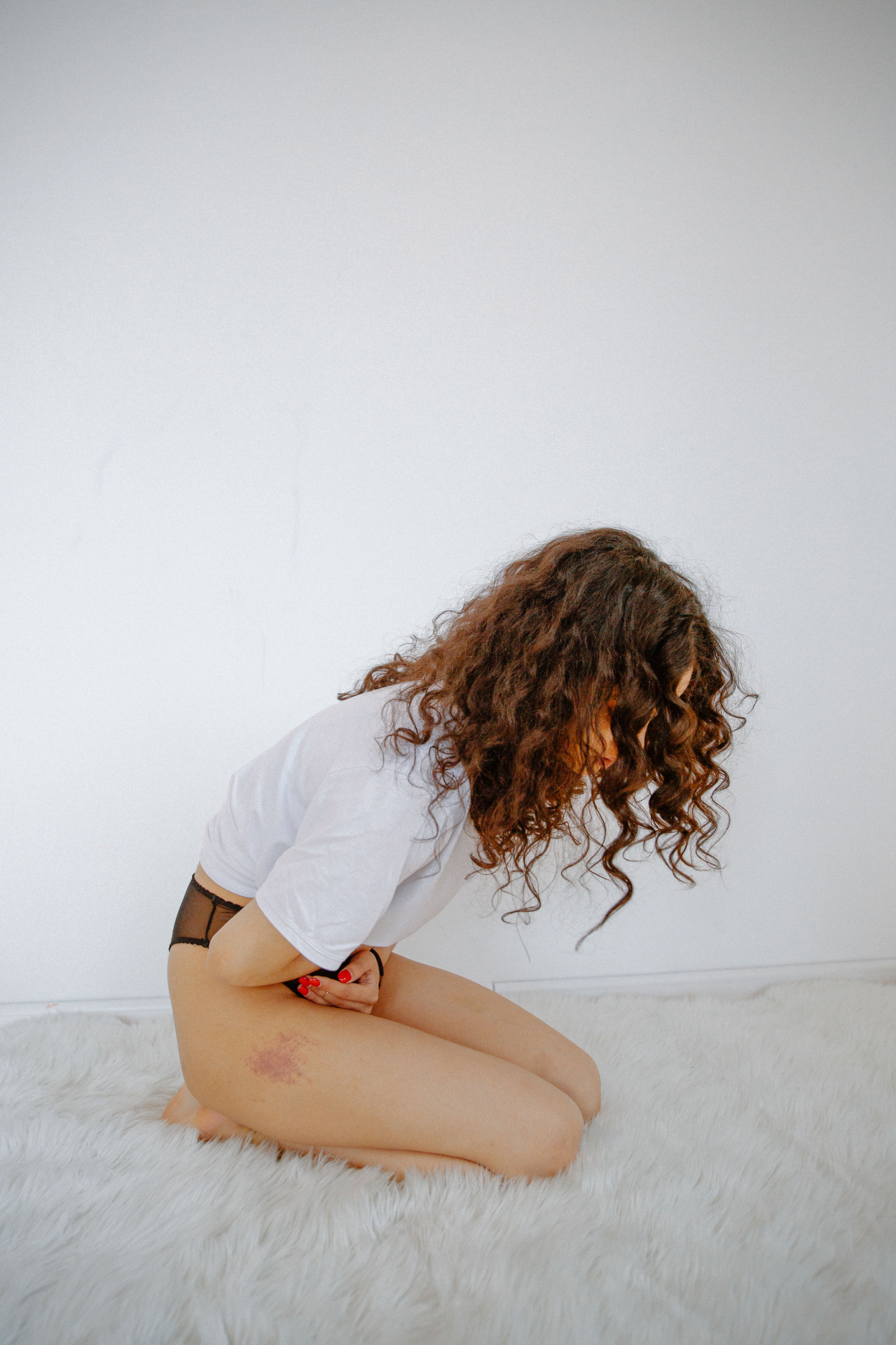 A woman kneeling on a soft white rug, pausing through period discomfort at home